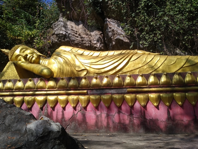 Golden reclining Buddha statue surrounded by nature.