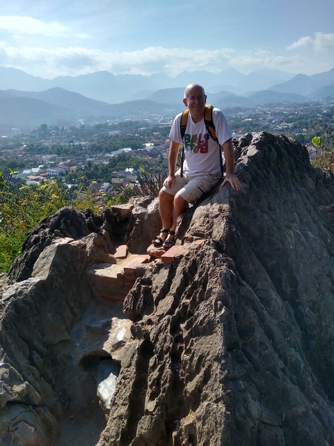 Person sitting on a rocky outcrop overlooking a cityscape.