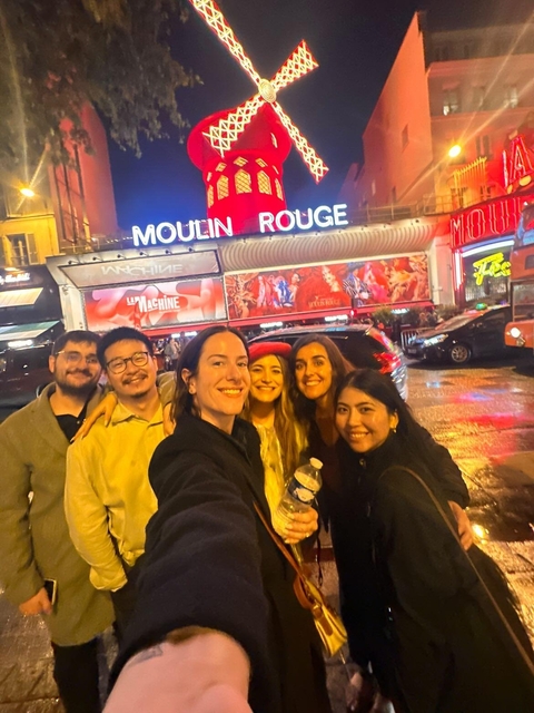 Group selfie outside the Moulin Rouge during the evening.