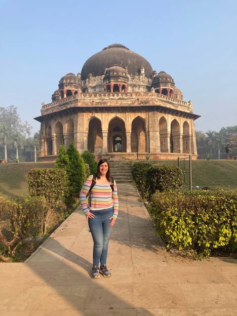 Person posing in front of a historic monument with arches.