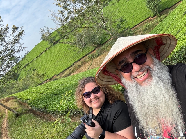 Two people in traditional hats posing in a green tea plantation.