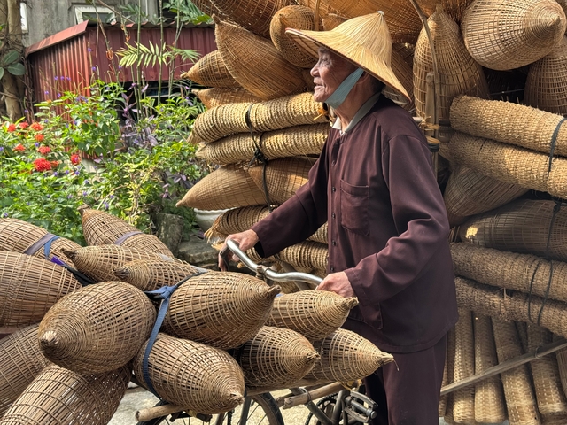 Old man with a traditional hat pushing a bicycle loaded with baskets.
