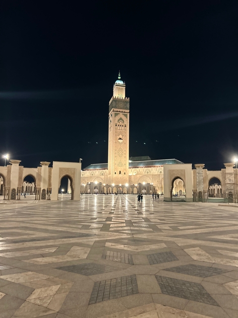 A night view of an ornate mosque with a large courtyard.
