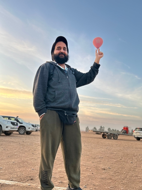       A man gesturing with the sky and vehicles in the background.
  