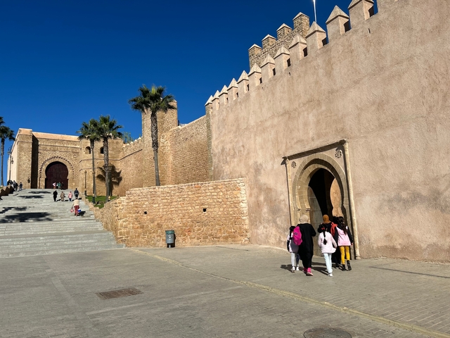       People walking near an ancient wall.
  