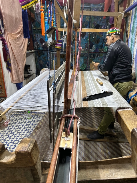       Person weaving on a loom in a colorful shop.
  