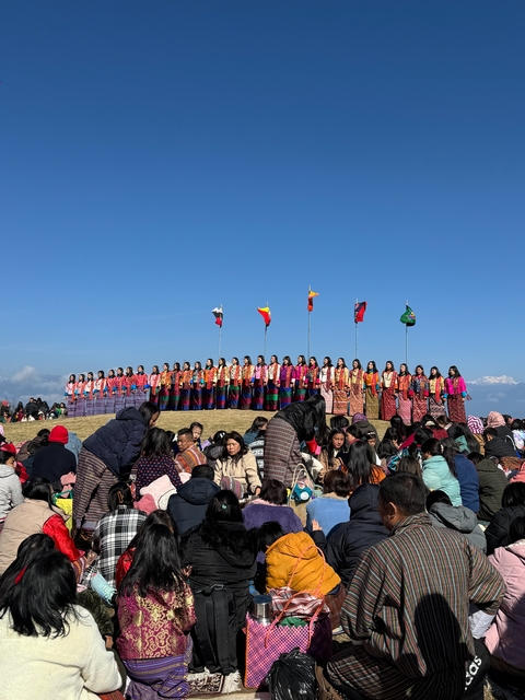 A cultural event with people in traditional Bhutanese attire and flags in a field.