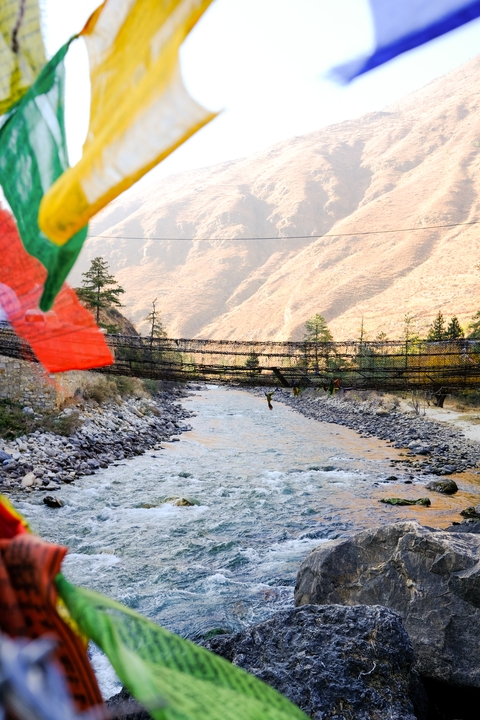 A suspension bridge over a river with colorful prayer flags in Bhutan.