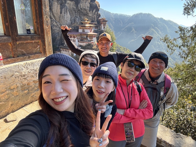 A group of tourists smiling for a photo with a Bhutanese monastery in the background.