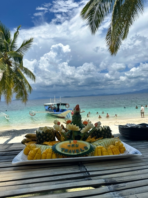       A bright beach scene with a boat, people swimming, and decorative fruit display.
  