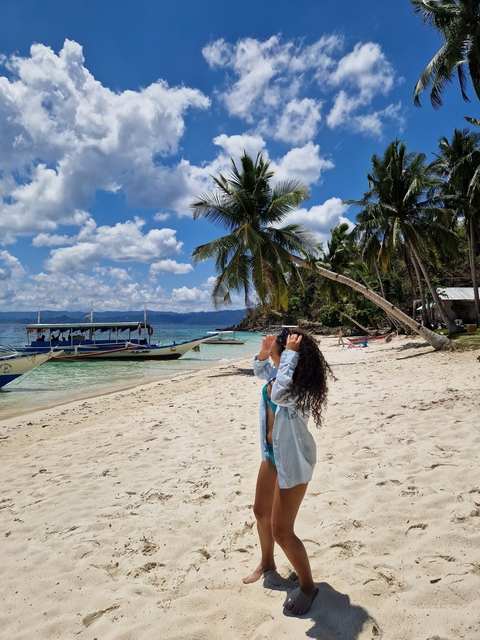       Person on a sandy beach with boats strung along the shore under palm trees.
  