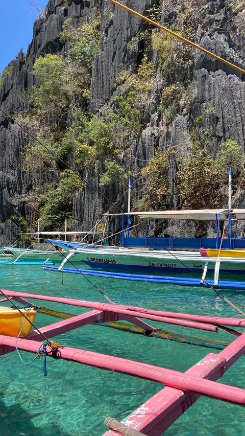       Colorful boats docked on clear water with rocky cliffs in the background.
  