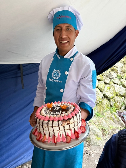 A chef holding a cake at a campsite.