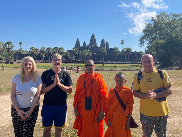       Group posing with monks in orange robes in front of Angkor Wat.
  