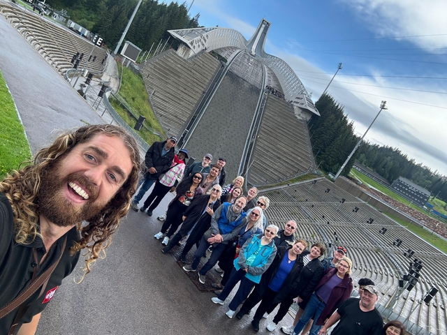       Group of people at a ski jump with a large structure in the background.
  