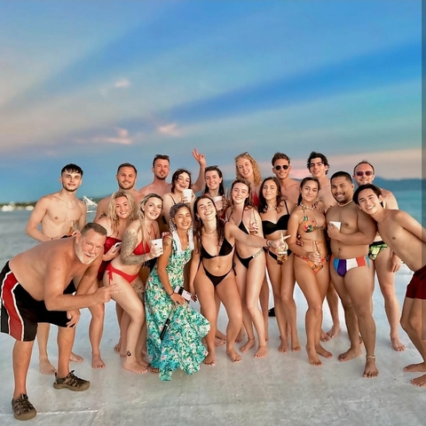       Large group of people posing on a beach in swimsuits.
  