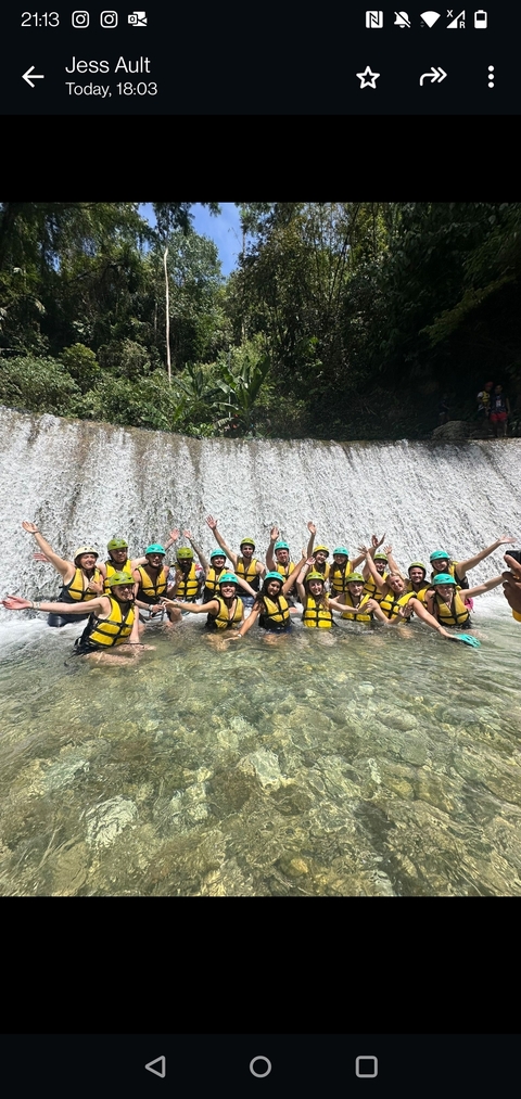       Group of people in life jackets enjoying themselves in front of a waterfall.
  