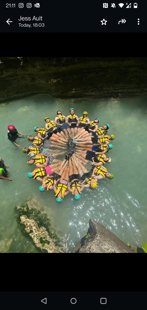       Group of people wearing life vests forming a circle in water.
  