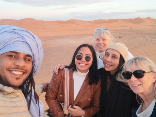       Group of friends taking a selfie with desert dunes in the background.
  