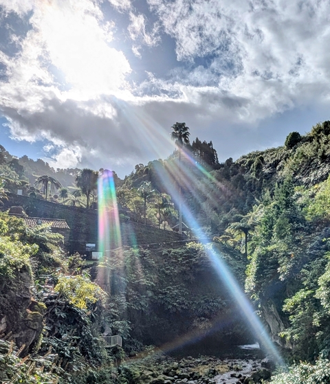 A hillside with rainbow-colored light rays breaking through the clouds.