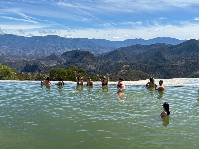Group of people enjoying a hot spring with a mountainous view.