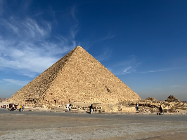 Large pyramid under a bright blue sky with people walking around.
