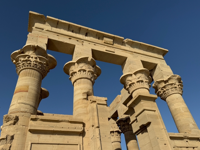 Ancient temple columns with detailed carvings against a clear blue sky.