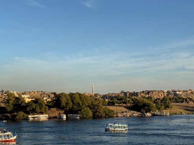 View of a river with boats and a distant mosque in a rocky landscape.