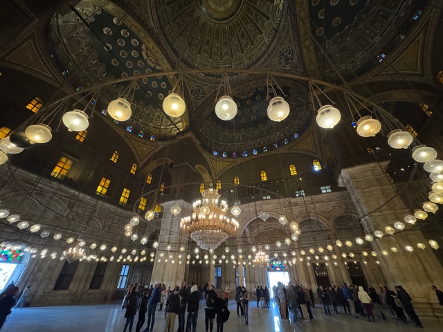       Beautifully lit interior of a mosque with large chandeliers and intricate decorations.
  