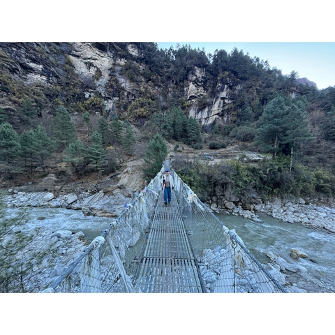       A person standing on a suspension bridge crossing a mountain river.
  