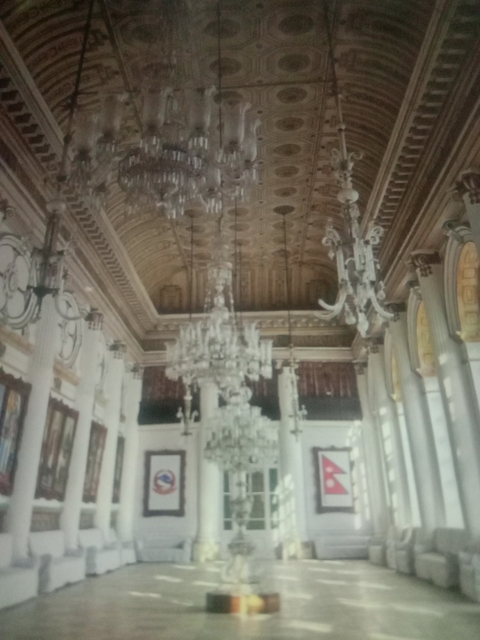 Interior of a grand hall with chandeliers and columns.