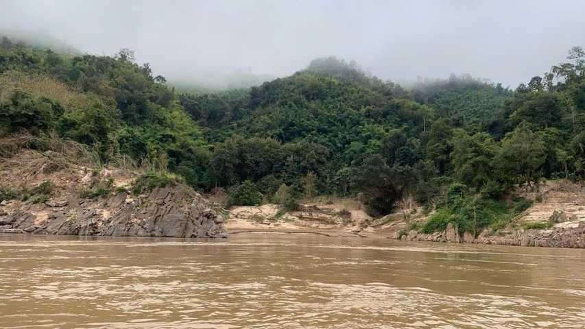 Misty forested hills beyond a brown river.