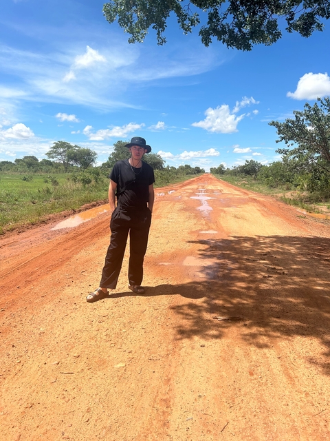 Person standing on a dirt road with trees in the background.