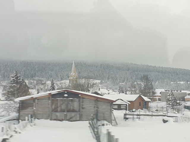       Snowy village landscape with a church tower.
  
