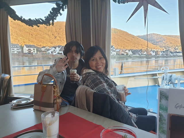       Two people sitting by a window on a boat with scenic views.
  