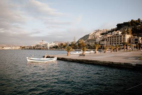 Seaside promenade with a boat and buildings lining the shore.