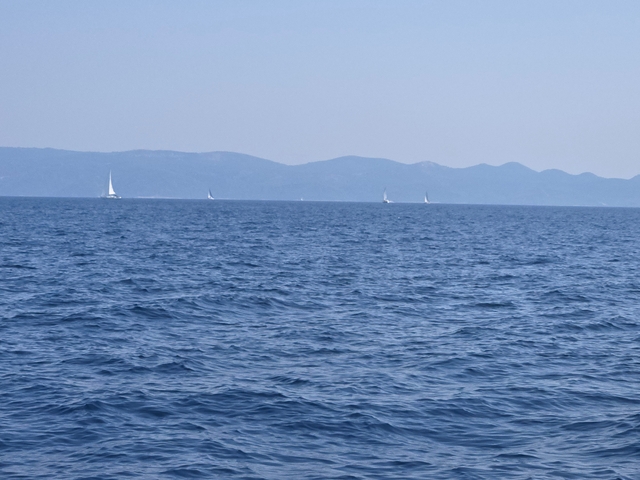 Distant sailboats on the sea with mountains in the background.