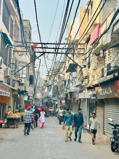 A bustling street with many people, shops, and electric wires overhead.
