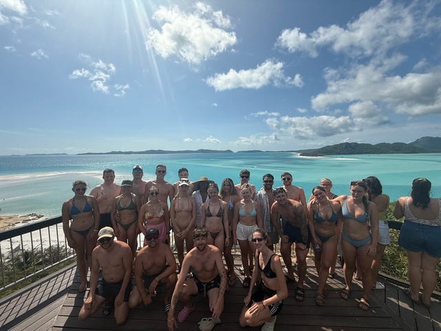       Large group of people posing at a beach viewpoint.
  