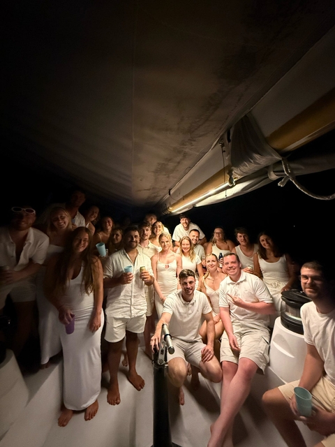 Group of people in white attire on a boat at night.