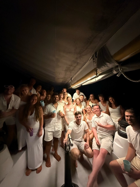       Group of people in white attire on a boat at night.
  