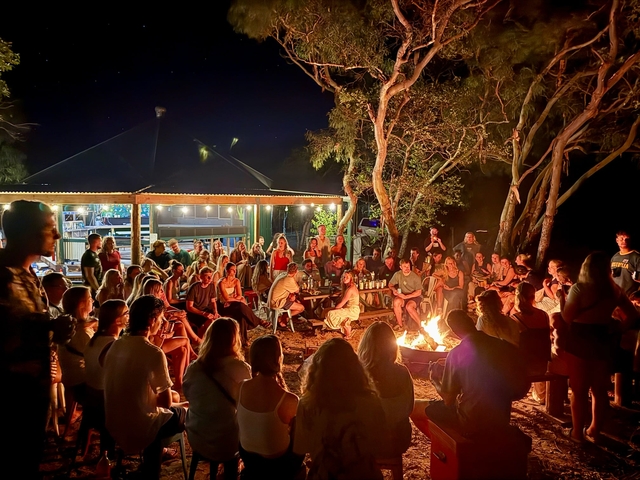Large group sitting around a campfire at night.