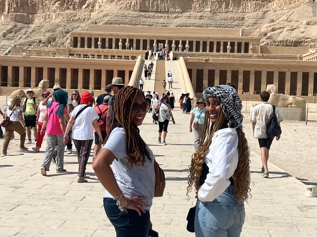       Two people posing in front of an ancient temple with others around.
  