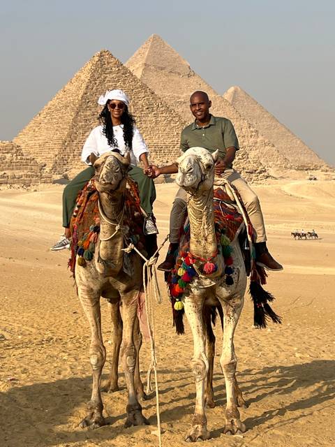       Couple riding camels with the pyramids in the background.
  