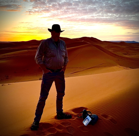       A person standing on sand dunes during sunset.
  