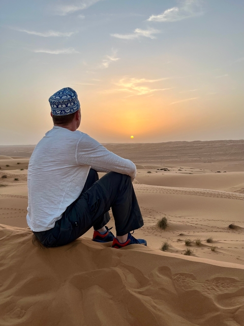 A man sitting on desert dunes watching the sunset.