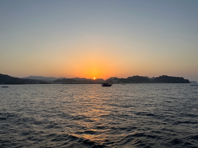 Sunset over a body of water with a boat silhouetted in the foreground.