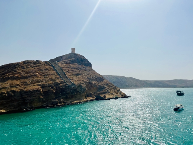 A rocky hill with a small tower overlooking a bright blue ocean.