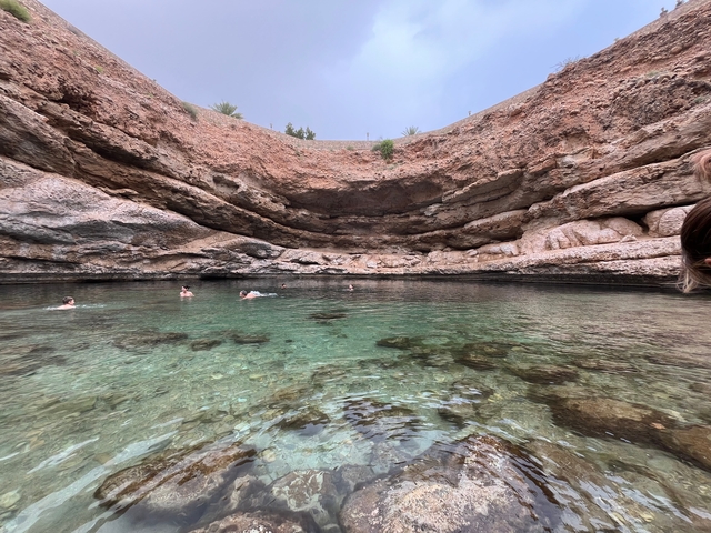 People swimming in a natural water pool surrounded by rocky cliffs.
