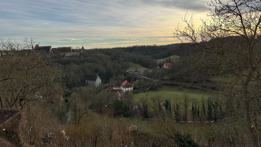 Countryside view with fields, houses, and a bridge at sunset.